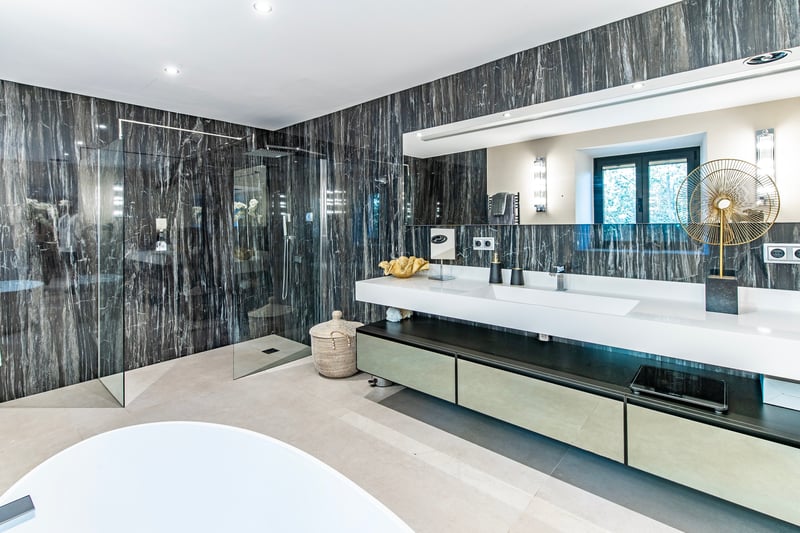 Salle de bains de luxe avec murs en marbre sombre, douche à l'italienne et double vasque suspendue.