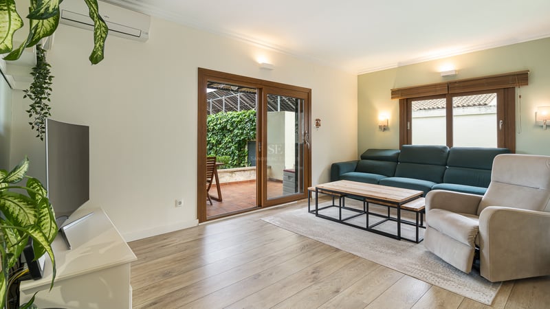 Salon lumineux avec canapé bleu canard, fauteuil, parquet et portes vitrées ouvrant sur une terrasse verdoyante.