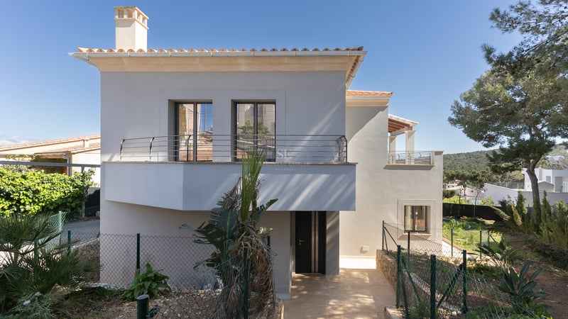 Villa moderne de deux étages avec façade blanche, tuiles en terre cuite et balcon sous un ciel bleu clair.