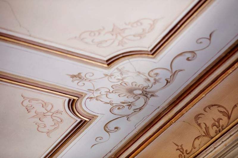Molduras de techo ornamentadas con filigrana floral pintada a mano en crema y oro.