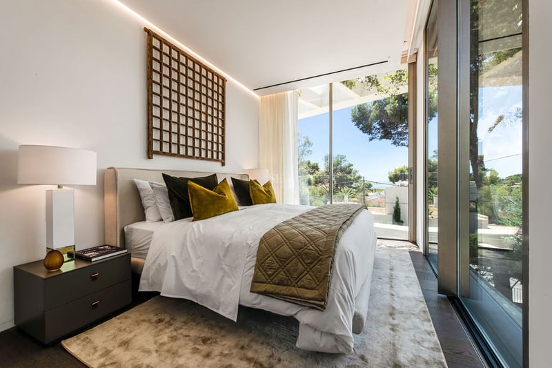 Chambre moderne avec grandes baies vitrées, coussins en velours et décoration murale en treillis de bois.