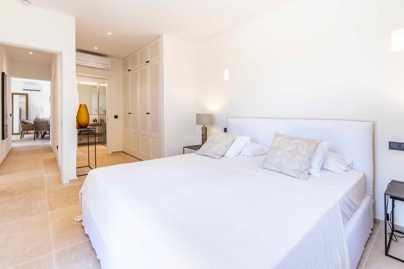 Bright master bedroom with white linens, custom perforated wardrobes, and a view into the ensuite bathroom.