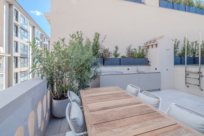 Terrasse moderne sur le toit avec table en bois, kitchenette extérieure et jardinières sous un ciel bleu.