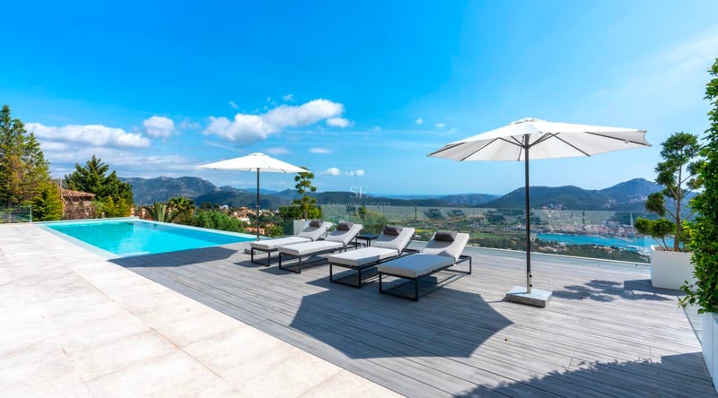 Piscine à débordement sur terrasse en bois avec bains de soleil gris, parasols blancs et vue mer et montagne.