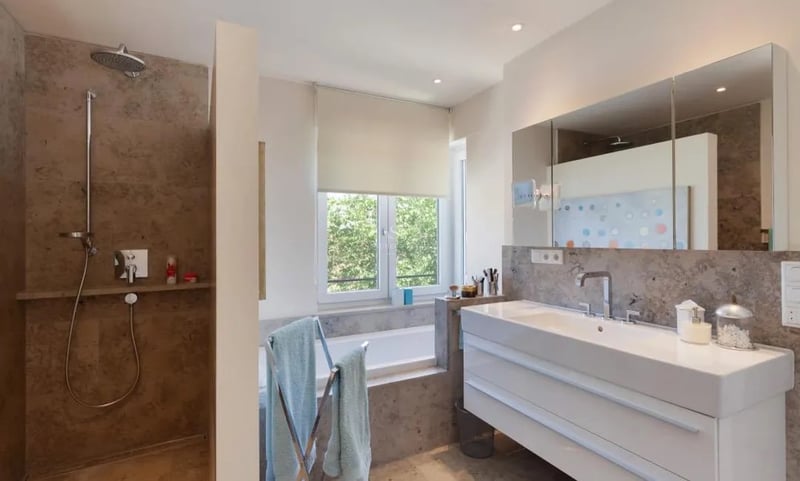 Salle de bains contemporaine avec douche à l'italienne en pierre, grand meuble vasque et baignoire sous fenêtre.