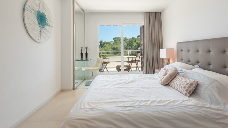 Chambre contemporaine lumineuse avec bureau en verre, tête de lit en cuir et accès direct à un balcon privé.