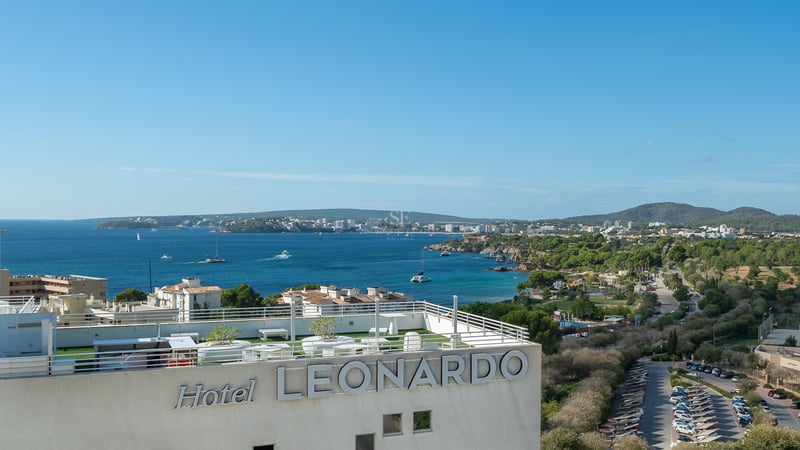 Vue panoramique d'une baie méditerranéenne et du littoral depuis un toit-terrasse moderne avec garde-corps blancs.