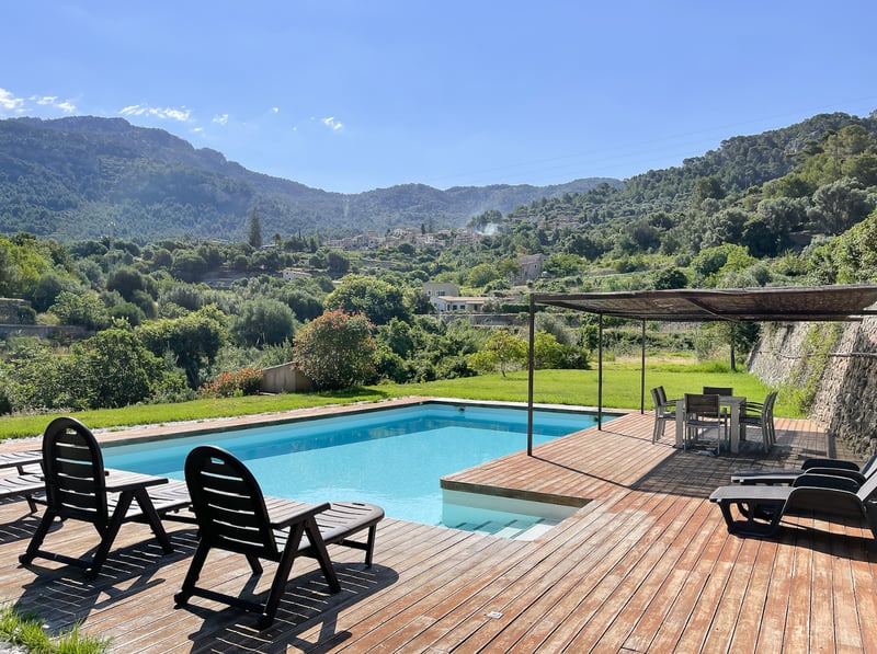 Piscine rectangulaire entourée d'une terrasse en bois avec transats et coin repas ombragé sous une pergola.