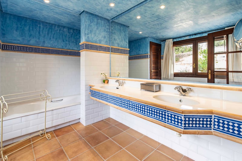 Salle de bain avec plafond bleu texturé, sol en terre cuite, double vasque et baignoire encastrée.
