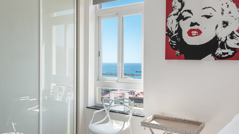 Chambre blanche lumineuse avec fenêtre sur mer Méditerranée, placards laqués et chaise design blanche.