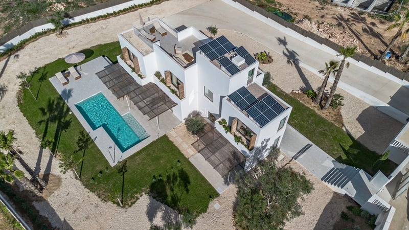 Vue aérienne d'une villa blanche contemporaine avec piscine, panneaux solaires et jardins paysagers.