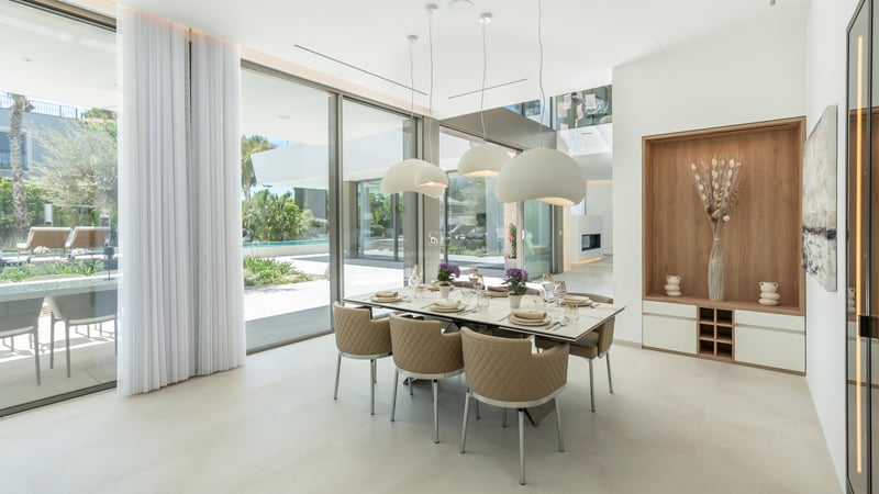 Salle à manger moderne avec grande table, chaises en cuir beige et baies vitrées donnant sur une piscine.