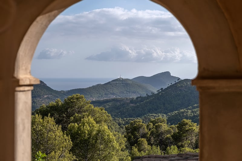 Vue de montagnes verdoyantes et de la mer au loin encadrée par une arche en pierre traditionnelle.