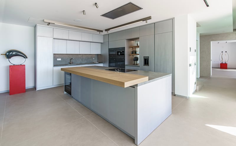 Cuisine moderne avec îlot gris, bar en bois, appareils intégrés et plans de travail en pierre grise.