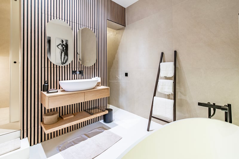 Salle de bains minimaliste avec mur en tasseaux de bois, deux miroirs ovales et meuble vasque suspendu en chêne.