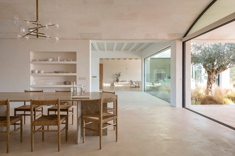 Modern dining area featuring a stone table, woven chairs, and large glass doors opening to a Mediterranean courtyard.