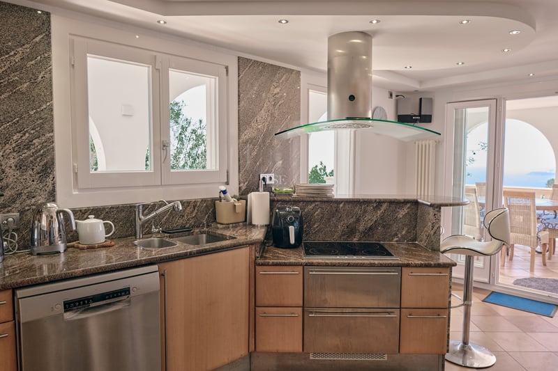 Cuisine contemporaine avec plans de travail en granit, appareils en inox et vue sur une terrasse ensoleillée.