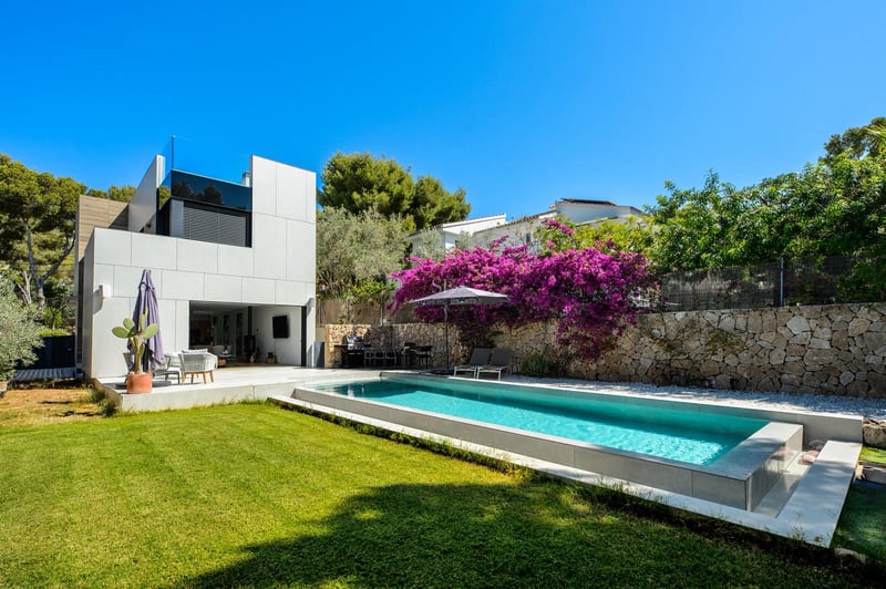 Piscine rectangulaire moderne à côté d'une villa blanche avec bougainvilliers violets et pelouse verte.