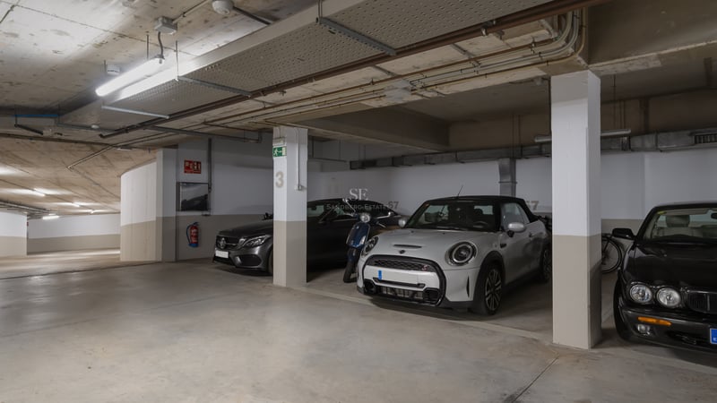 Garage souterrain lumineux avec places numérotées, piliers en béton et voitures de luxe stationnées.