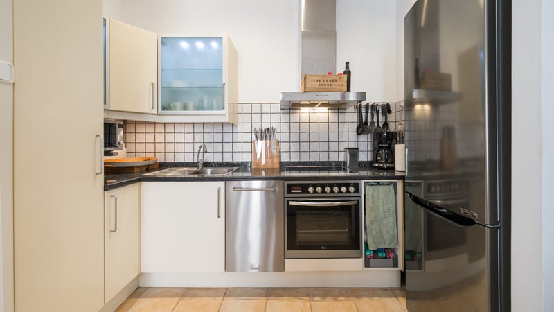 Cuisine moderne avec placards crème, électroménager en inox, plan de travail en granit noir et crédence en carrelage blanc.