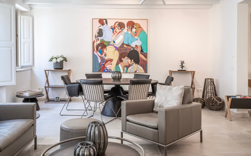 Pièce moderne lumineuse avec un fauteuil en cuir gris, une table à manger ronde et un grand tableau coloré au mur.
