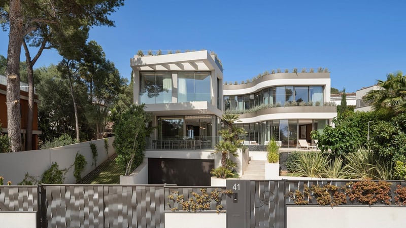 Villa contemporaine blanche de trois étages avec parois de verre courbes et entrée sécurisée sous un ciel bleu.