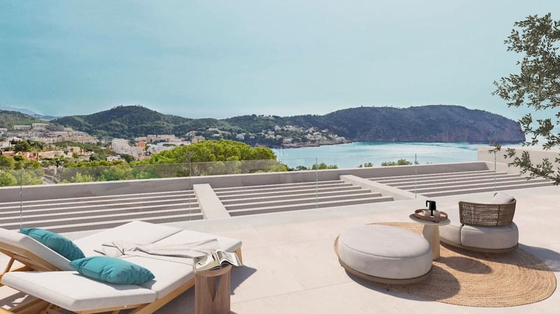 Terrasse moderne en pierre avec chaises longues et mobilier design surplombant une baie méditerranéenne et des montagnes.