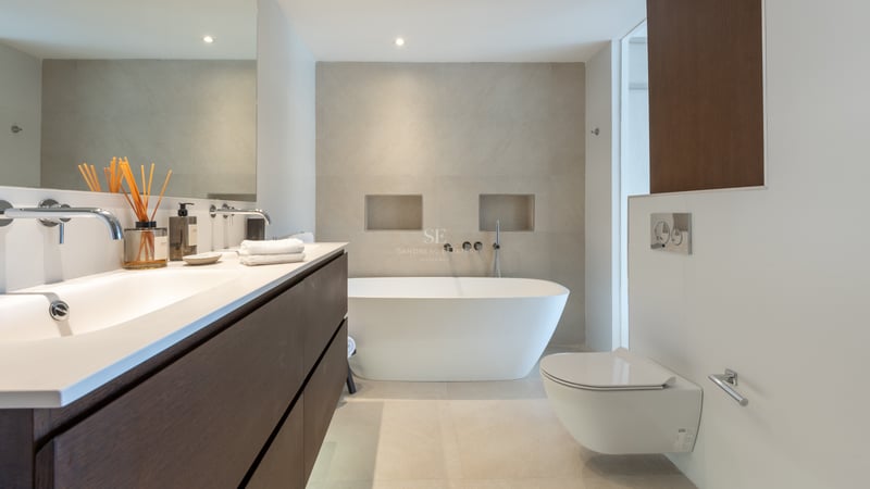 Salle de bains minimaliste avec baignoire îlot blanche, meuble en bois foncé et carrelage beige.