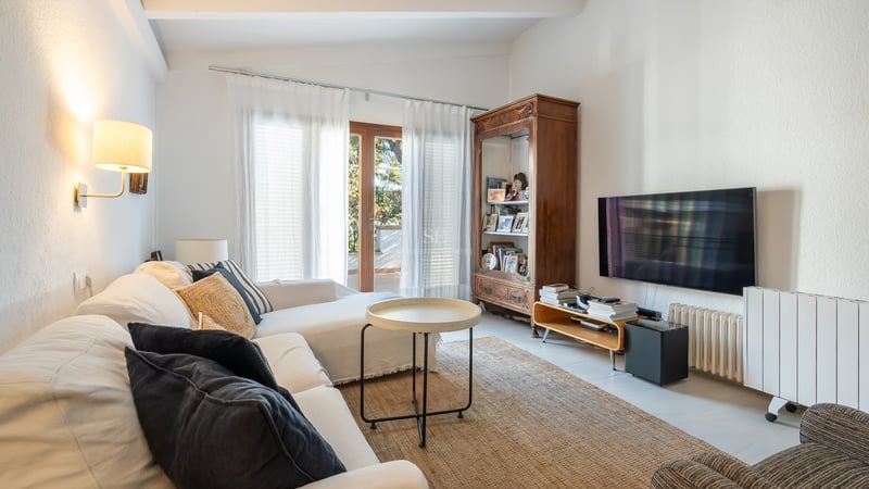 Salon lumineux avec canapés blancs, une grande armoire en bois, une télévision murale et un accès terrasse.