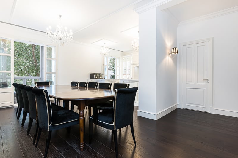 Grande table en bois foncé, chaises en velours noir et lustres en cristal dans une pièce blanche lumineuse.