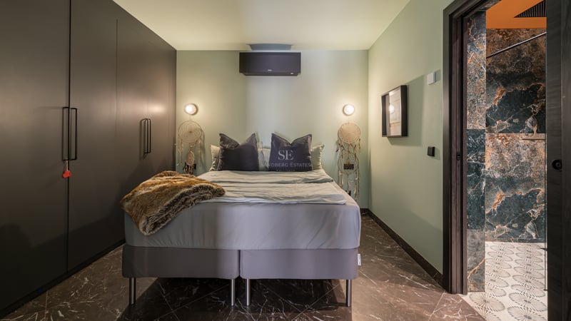 Chambre moderne avec murs vert sauge, sol en marbre sombre, placards intégrés et aperçu de la salle de bain attenante.