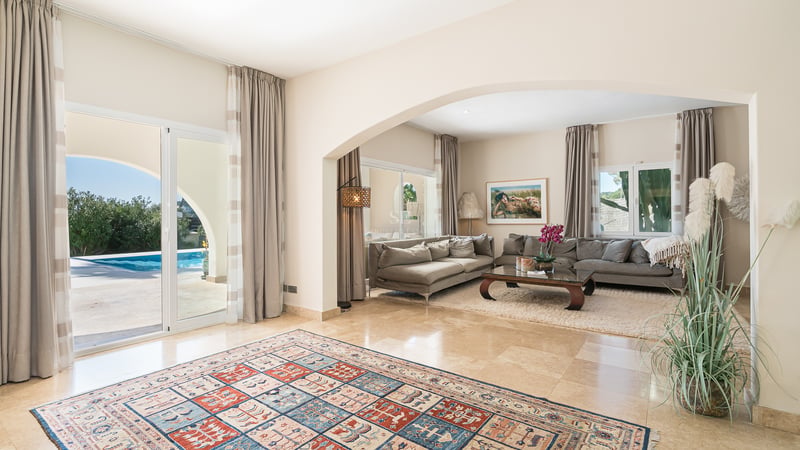 Grand salon moderne avec sol en marbre, canapés gris et baies vitrées ouvrant sur une piscine bleue.