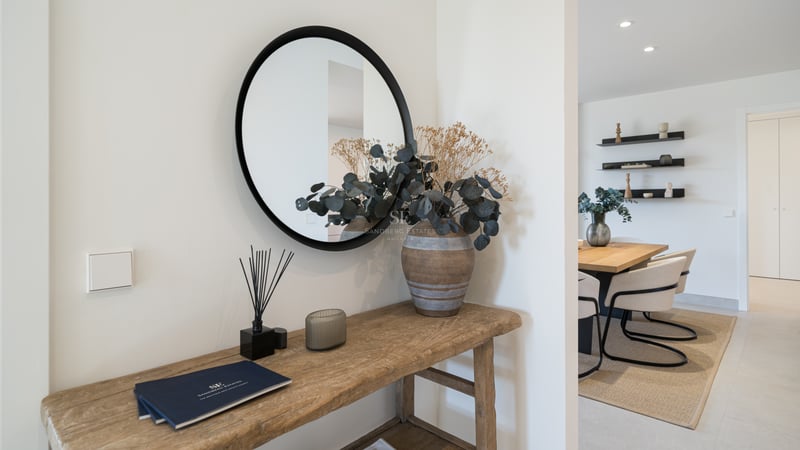 Entrada minimalista con consola de madera rústica, espejo circular negro y vistas al comedor moderno.