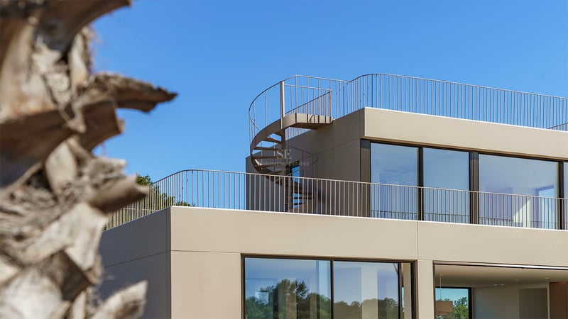 Détail architectural d'une villa beige contemporaine avec un escalier en colimaçon menant au toit sous un ciel dégagé.