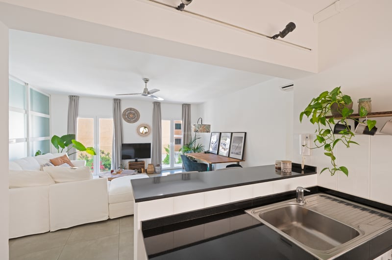 Vue depuis le comptoir de cuisine vers un salon clair avec canapé blanc, coin repas et portes vitrées.
