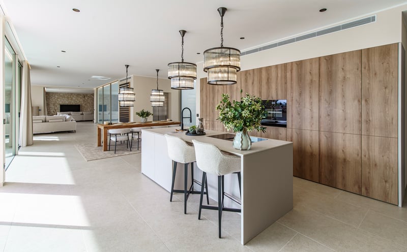 Cuisine moderne avec un grand îlot, tabourets blancs, suspensions design et armoires en bois dans un espace ouvert.
