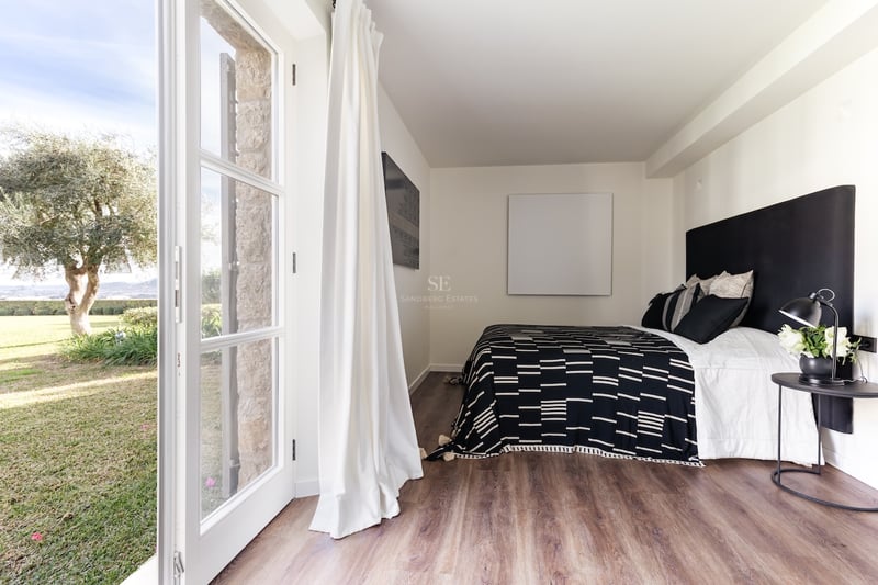 Chambre contemporaine avec parquet, lit double et grandes portes vitrées ouvrant sur un espace extérieur.
