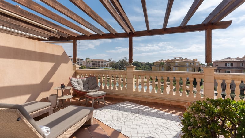 Terrasse privée ensoleillée avec pergola en bois, balustrade en pierre et coin salon donnant sur le quartier.