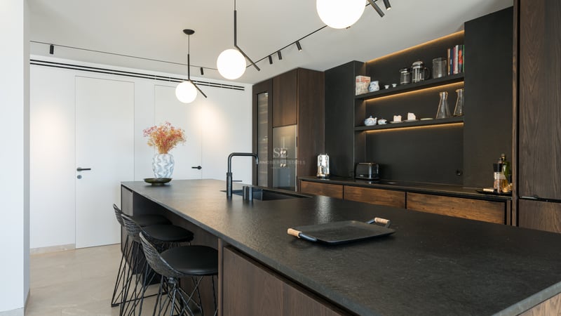 Cuisine contemporaine dotée d'un îlot en pierre noire, de placards en bois sombre et de suspensions sphériques.