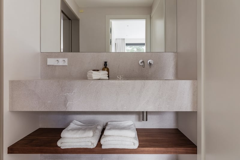 Gros plan d'un lavabo en pierre suspendu avec étagère en bois et serviettes blanches pliées.