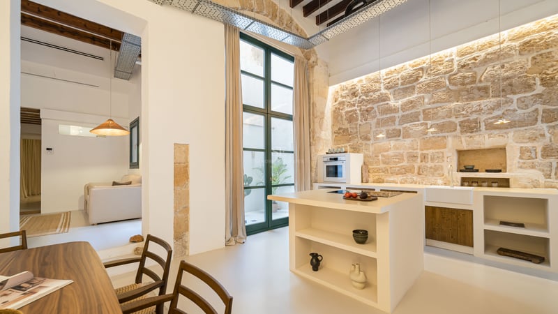 Cuisine moderne avec mur en pierre rustique, îlot blanc et poutres en bois au plafond.