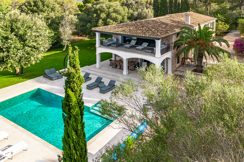 Vue surélevée d'une villa en pierre avec piscine turquoise, bains de soleil et jardins verdoyants.