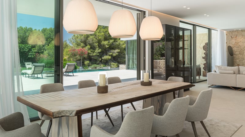 Salle à manger moderne avec table en bois naturel et chaises rembourrées donnant sur une piscine à travers des baies vitrées.