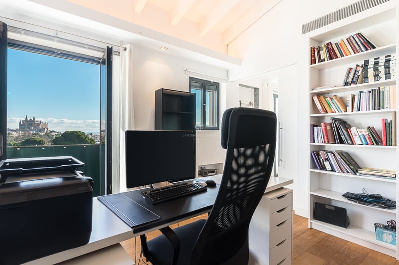 Bureau moderne avec bureau, chaise ergonomique et grande bibliothèque face à une fenêtre donnant sur la cathédrale.
