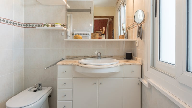 Vanité de salle de bain crème avec plan de travail en marbre, lavabo semi-encastré et bidet à côté d'une fenêtre.