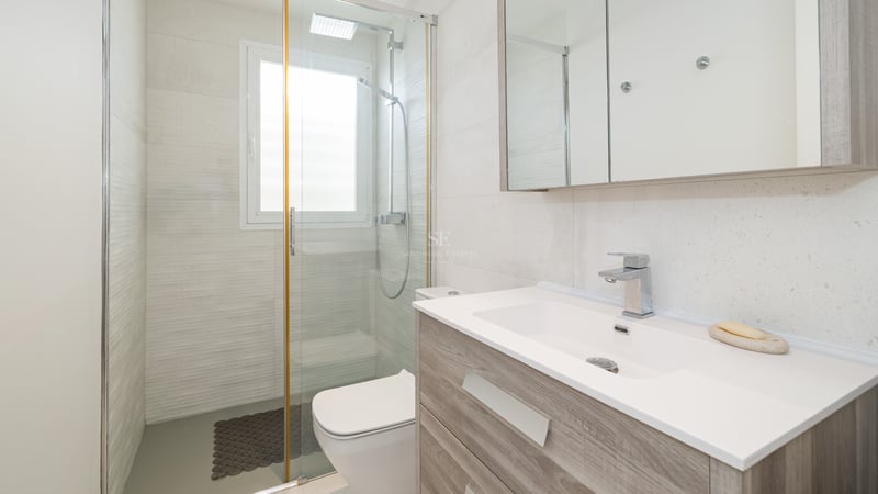 Salle de bain lumineuse avec meuble vasque en bois, grand miroir et douche vitrée.