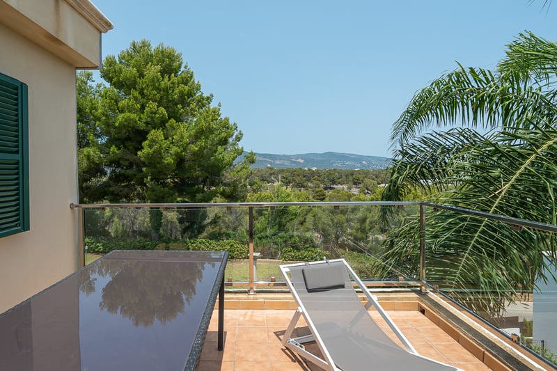 Terrasse en terre cuite avec chaise longue et garde-corps en verre offrant une vue sur une forêt de pins.
