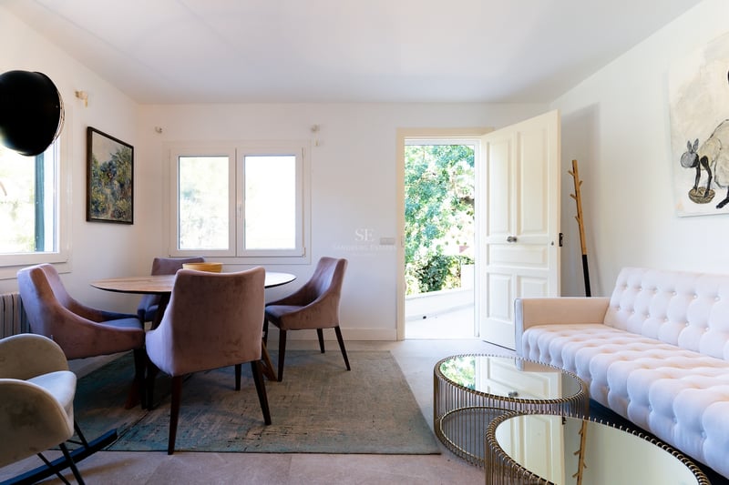 Salon lumineux avec canapé capitonné blanc, tables basses en miroir et coin repas avec chaises en velours.