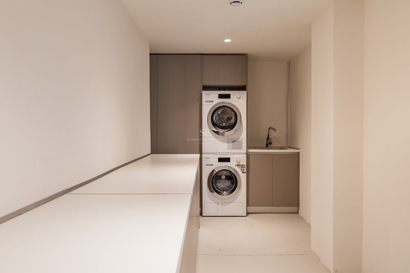 Lave-linge et sèche-linge Miele superposés dans une buanderie minimaliste avec placards taupe et plan de travail blanc.