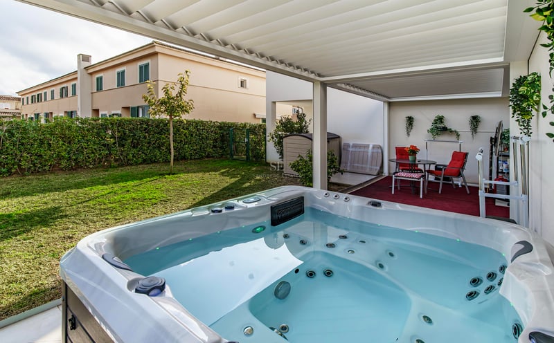 Jacuzzi de luxe blanc sous une pergola bioclimatique donnant sur un jardin privé avec des chaises rouges.
